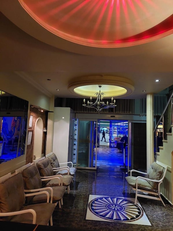 Un vestíbul d'hotel amb taulell de recepció, zona de seients i un penjall de cristall.