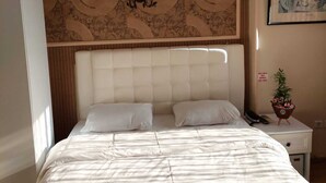 A hotel room with a large bed, a headboard with a decorative panel, a nightstand with a phone and a plant, and a framed picture on the wall. - GOLDEN ELİT OTEL (Bandirma)