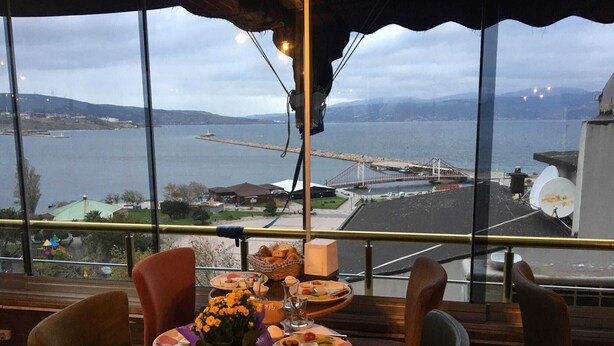 A table set for dining with a view of a body of water and a bridge in the background. - GOLDEN ELİT OTEL (Bandirma)
