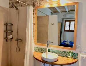 A bathroom with a wooden vanity, a round sink, a shower with a handheld showerhead, and a mirror with a wooden frame.