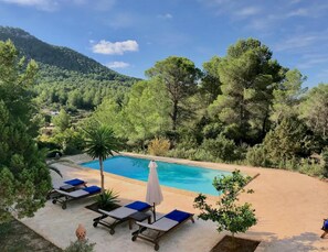 A pool area with lounge chairs and umbrellas, surrounded by trees and a mountain in the background. - Villa With Private Pool (Sant Cebria de Vallalta)