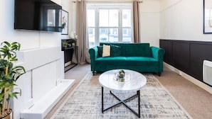 Ein modernes Wohnzimmer mit einem salbeigreenen Sofa, einem runden Couchtisch und einem flachbildfernseher, der an der Wand montiert ist.