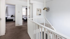Ein Flur mit weißer Geländer, einer Treppe und einer Tür zu einem Schlafzimmer mit Bett und Nachttisch.