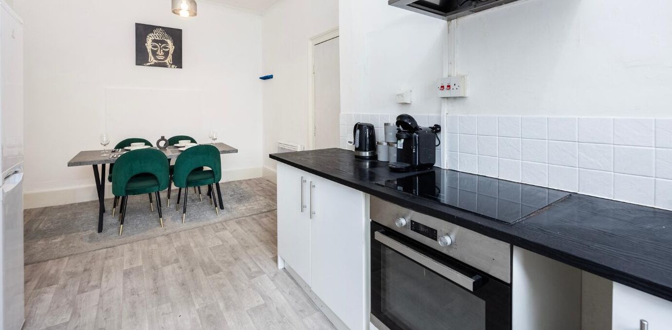 A compact kitchen with a black countertop, a built-in oven, and a dining area with two green chairs and a small table.