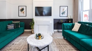 Ein modernes Wohnzimmer mit zwei grünen Sofas, einem Marmortisch, einem Flachbildfernseher und gerahmten Kunstwerken an den Wänden.