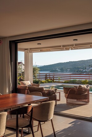 A modern outdoor dining area with a wooden table and chairs, overlooking a scenic lake and hills. - Villa Remi (Selca)