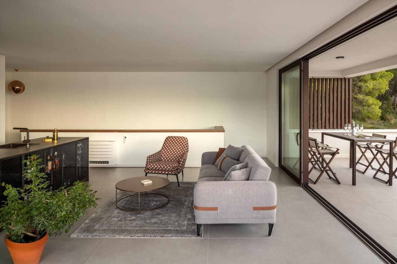 A modern living room with a sofa, armchair, and coffee table, a kitchen area with a black cabinet, and a dining area with a table and chairs.