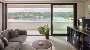 Ein modernes Wohnzimmer mit einer Couch, einem kleinen Tisch, einer Topfpflanze und einem Glasvitrine mit Flaschen.