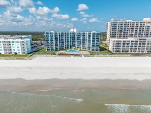 A beachfront hotel with multiple floors, a swimming pool, and a view of the ocean.