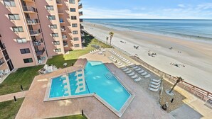 A swimming pool with lounge chairs, a beach, and a high-rise building.