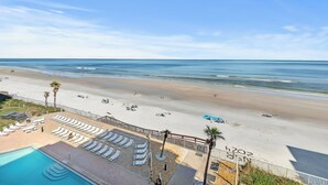 A beach view with a pool area, lounge chairs, and a fenced deck.
