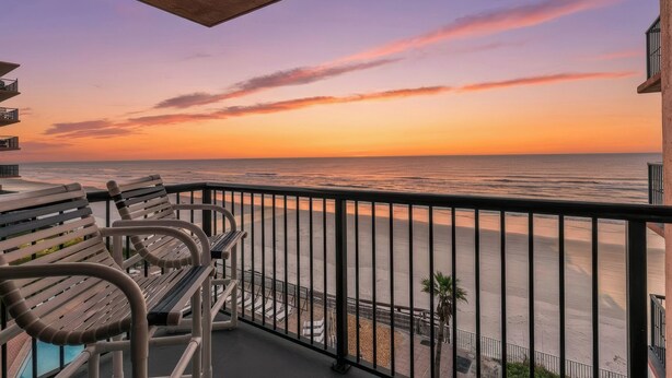 A balcony with a view of the ocean at sunset.