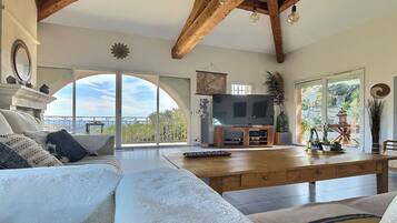 Een ruime woonkamer met een grote televisie, houten balken en een balkon met uitzicht.