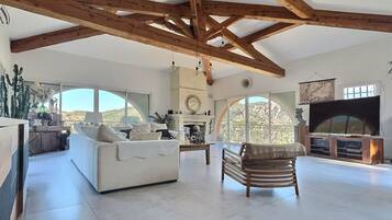 Amplia sala de estar con techo alto, chimenea, televisor grande y vistas al exterior.