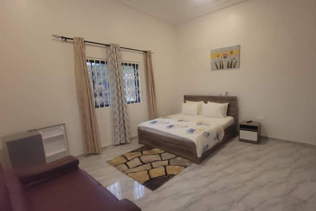 A bedroom with a bed, bedside table, TV, and a window with curtains.