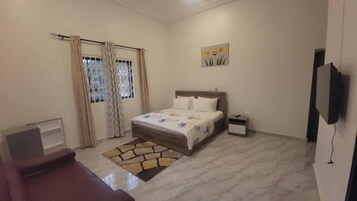 Quarto com cama, mesa de cabeceira, televisão e janela com cortinas.