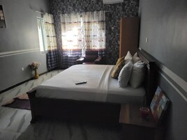Quarto com cama, mesa de cabeceira, cadeira, janela com cortinas e parede com desenho estampado.
