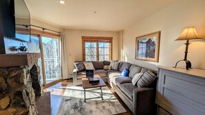 A cozy living room with a stone fireplace, a large window, and a sofa set. - Pool/Hot Tub/Views, Walk to River Run Festivals (Keystone)