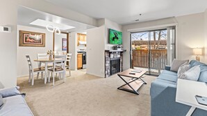 Ein modernes Wohnzimmer mit Sofa, einem Esstisch mit Stühlen, einem Kamin und einer Küche im Hintergrund.