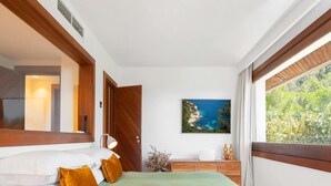 Ein Schlafzimmer mit einem Bett, einem Nachttisch, einem Gemälde und einem Fenster mit Blick auf Grünflächen.