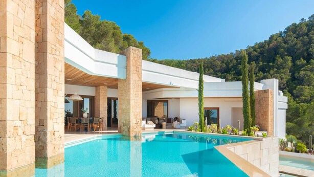 Ein moderner Poolbereich mit Steinsäulen, einem klaren Pool und Blick auf den umliegenden Wald.