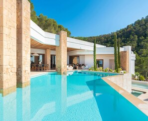A modern poolside area with stone pillars, a clear pool, and a view of the surrounding forest.