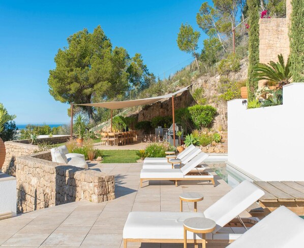 A rooftop terrace with lounge chairs, a dining area, and a view of the sea.