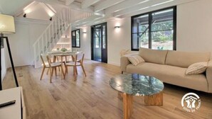 A modern living room with a wooden floor, a round coffee table, a beige sofa, and a staircase with white railings.