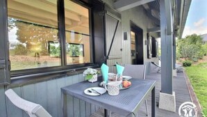 An outdoor patio with a table set for two, a chair, and a window with blinds.
