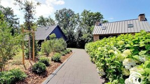 A pathway leading to a building with a metal roof, surrounded by greenery and trees.