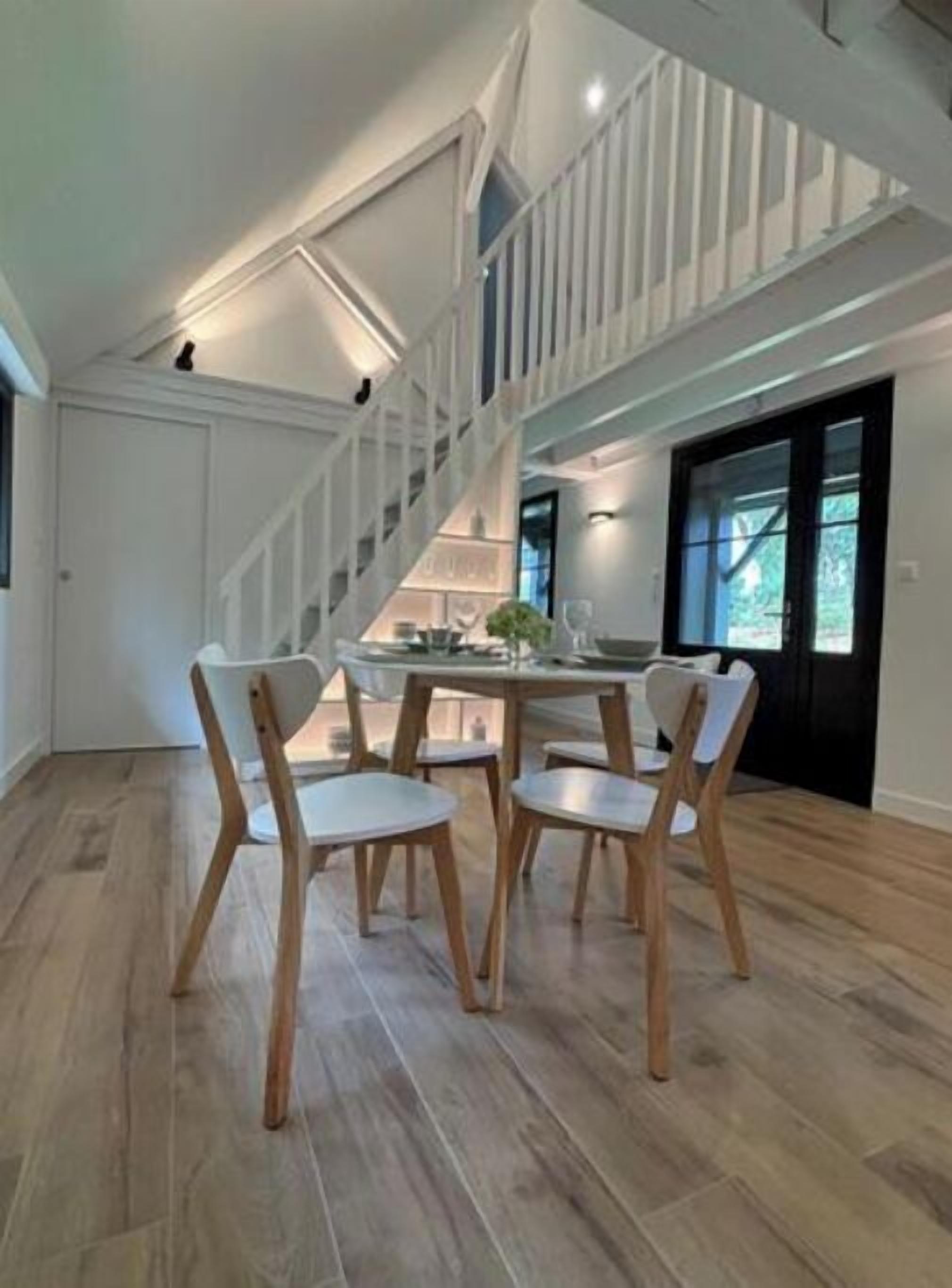 Une pièce spacieuse avec un plafond haut, un escalier menant à un niveau supérieur et un coin repas comprenant quatre chaises et une table.