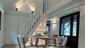 A spacious room with a high ceiling, a staircase leading to an upper level, and a dining area with four chairs and a table.