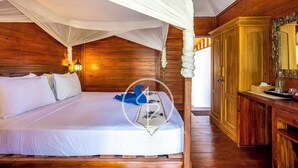 A wooden four-poster bed with white bedding, a bedside lamp, and a wooden dresser with a mirror. - Ings Garde (Gili Air)