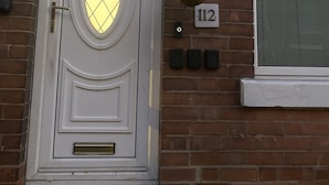 A white door with a glass panel, a number plate '112', and a hanging flower basket.