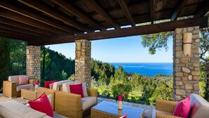 A covered outdoor seating area with wicker furniture and stone pillars, overlooking a scenic landscape with a view of the sea. - Traditional Villa With Private Pool (Banyalbufar)