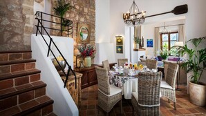 A dining area with wicker furniture, a chandelier, and a stone wall. - Traditional Villa With Private Pool (Banyalbufar)