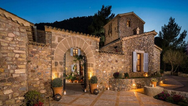 A stone building with an arched entrance, a small tower, and a courtyard with potted plants and outdoor lighting. - Traditional Villa With Private Pool (Banyalbufar)