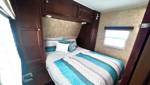 Quarto compacto de motorhome com cama, armários embutidos e janela.