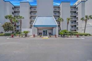 A multi-story hotel with a central entrance, surrounded by palm trees and a landscaped area.