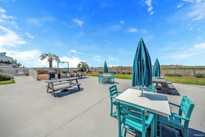 An outdoor patio area with picnic tables and chairs, a barbecue grill, and umbrellas. - FREE Golf & Perks! Mariner West 306- Low Floor, Pool, Tennis & BBQ Grills! (Panama City Beach)