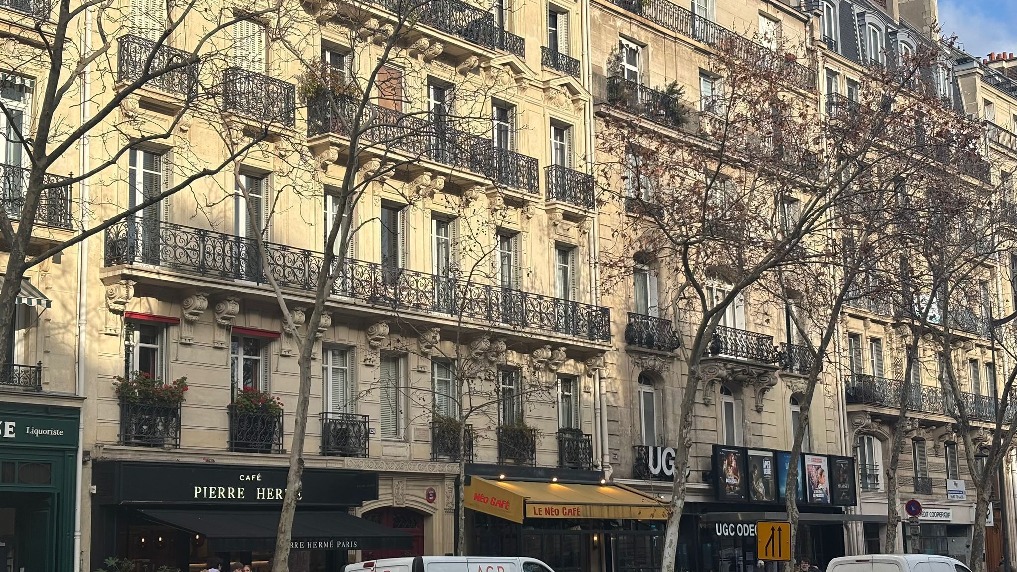 A multi-story building with ornate balconies and storefronts, including a café and a liquor store.