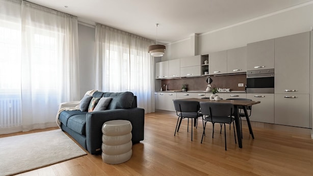 A modern living room with a sofa, a dining table with chairs, and a kitchen area with cabinets and appliances. - HouSmart Massarenti 61 (Bologna)