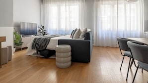 A modern bedroom with a bed, bedside table, TV, and a dining area with chairs. - HouSmart Massarenti 61 (Bologna)