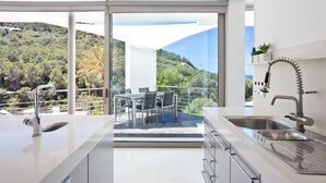 Una cucina moderna con una grande finestra, un'area pranzo con tavolo e sedie, e vista su una collina.