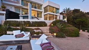 Una moderna casa a due piani con un patio attrezzato con sdraio e un tavolino.