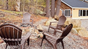 A cabin with a stone fire pit and Adirondack chairs in a forest setting. - Charming 2-bedroom house with AC, WiFi in tranquil Conway (Conway)