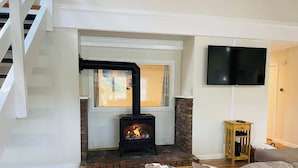 A living room with a wood-burning stove, a TV mounted on the wall, and a staircase leading to an upper level. - Charming 2-bedroom house with AC, WiFi in tranquil Conway (Conway)