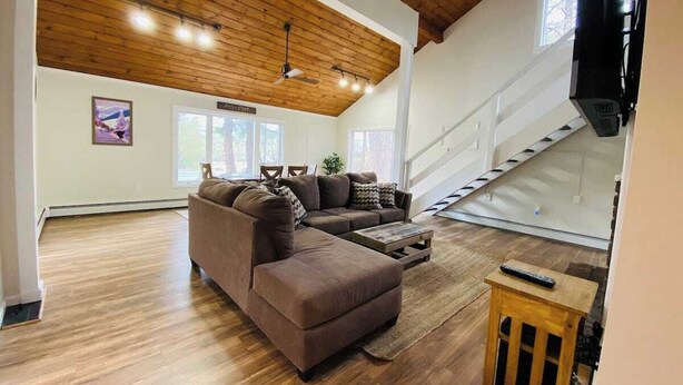 A spacious living room with a wooden ceiling, a sectional sofa, a wooden coffee table, and a staircase leading to an upper level. - Charming 2-bedroom house with AC, WiFi in tranquil Conway (Conway)