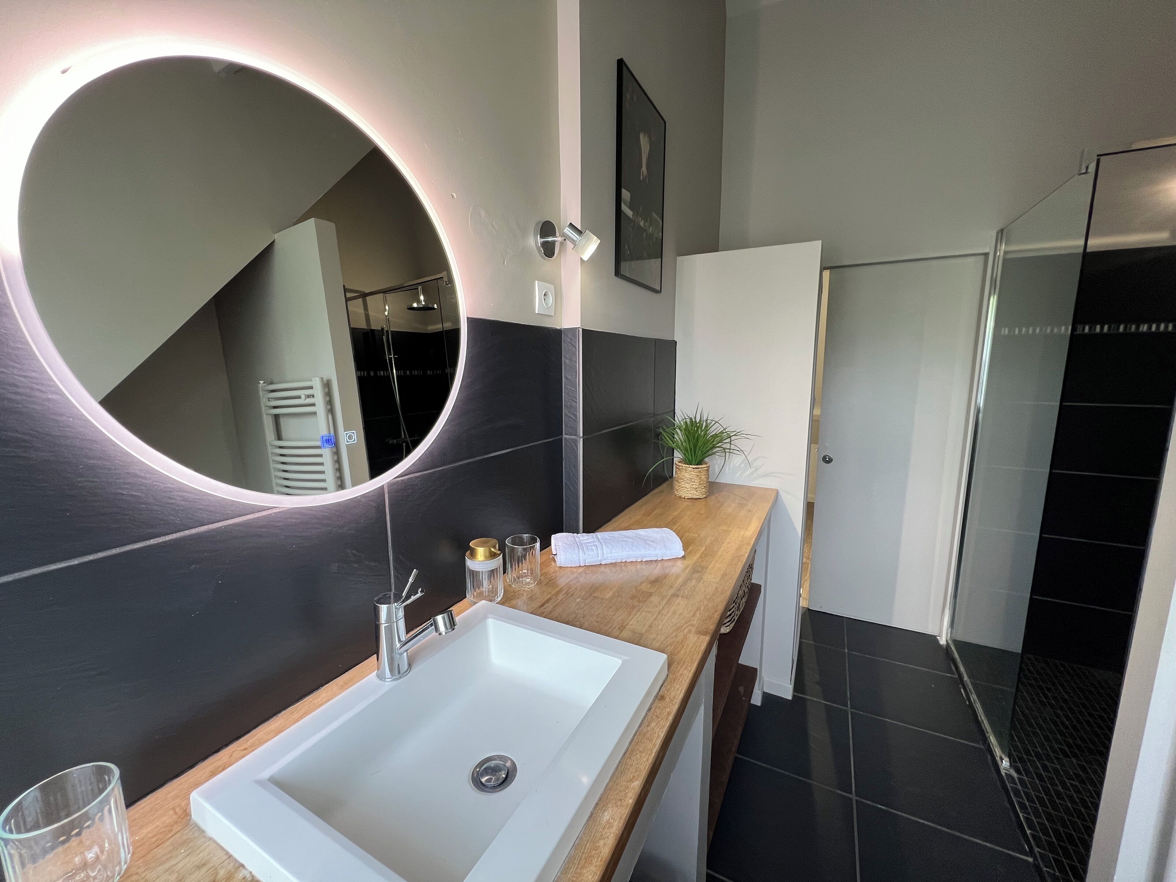 A modern bathroom with a large mirror, a white sink, and a shower area.