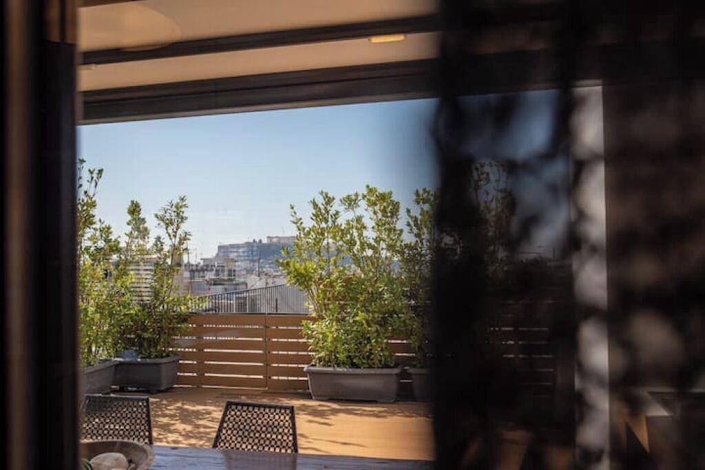 A balcony with potted plants, a wooden fence, and a view of buildings in the distance.